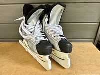 Front angle showing the pair of Bauer ice skates, white laces, black toe caps, and silver design.