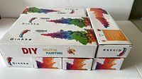 Eight white boxes of Ginkko DIY Digital Painting Kits stacked on top of each other showing colorful paint splash tree graphics and brand logo.