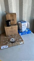 Four boxed and loose household items: Brita water filter jug, boxes of tin camping cups and plastic bowls, plus a decorative wall clock.