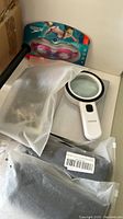 Photo shows Speedo goggles on packaging, white magnifier, black suspenders in plastic bag