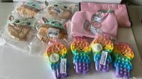 Photo of four Yoda character lunch bags in plastic packaging, two pink unicorn lunch bags with cartoon unicorn design, and four rainbow-colored Pop It fidget purses shaped like paws.