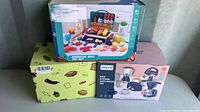 Three boxed kids play sets including a barbecue grill set, kitchen appliances set, and an unidentified green box set