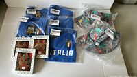 Photo showing six blue Italia baby onesies and three teething accessories in Christmas-themed boxes plus two summer hats in plastic bags.