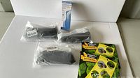 Lot showing three black foldable travel foot rests in plastic packaging, two packs of fly sticky pads with green and yellow color casing, and one boxed infrared forehead thermometer.