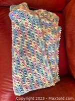 Multi-color pastel crocheted baby blanket folded on red couch, showing shell stitch pattern