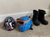 Two kid helmets and one pair of black winter boots displayed on carpet.