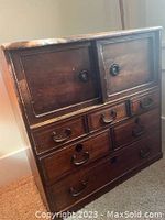 Full view of the small wooden Tansu chest showing multiple drawers, two sliding panels, and black metal fixtures.