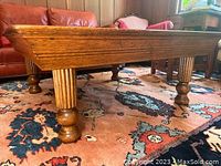 Side angled view of coffee table showing fluted round legs with turned ball feet and sturdy structure on a patterned rug.