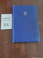 Top-side view of blue hardcover book with MaxSold lot number next to it, showing cover texture and condition