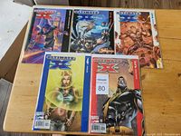 Five Ultimate X-Men comics issues 1 through 5 laid out on wooden surface, showing front covers with colorful character art including prominent X-Men figures.
