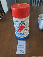 Front view of vintage NHLPA thermos showing red lid, NHL player silhouette logo, and printed player signatures.