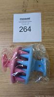 Two silicone hair scalp massager brushes, pink and blue, placed side by side in original clear packaging with auction lot tag.
