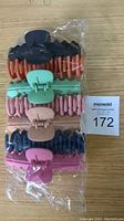 Packaged 7 hair claw clips in various colors displayed in sealed plastic wrap on wooden surface with MaxSold lot tag.