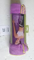 Purple yoga mat towel rolled with packaging showing a female model in yoga pose on front with product features and branding; purple fabric with yellow edged loop straps visible