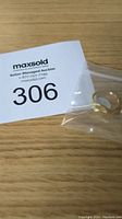Close-up photo of the gold signet ring in the plastic bag displayed with the Maxsold auction card number 306 on a wooden surface.