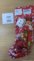 Front view of red Christmas stocking containing white mouse plush, brown teddy bear plush, red fuzzy ball and shiny balls inside clear packaging.