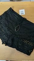 Black lace crochet bikini shorts laid flat on wood surface showing front and waistband detail with drawstring.