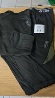 Black thermal underwear set including top and long johns laid out on a wooden surface, showing front view.