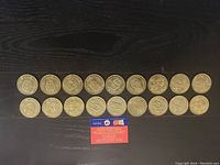 Photo of 20 Olympic-themed coins arranged in 2 rows on dark surface.