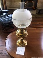 Full view of an antique brass oil lamp with frosted and etched glass shade, clear cylindrical chimney, and polished brass base, placed on a wooden table.