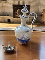 Photo showing porcelain liquor bottle and small Viking ship salt shaker on wood table.