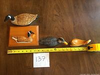 Four carved wooden ducks arranged on a wooden surface with measuring tape showing length about 12 inches.