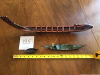 Three Viking vessel replicas shown on a wooden table with measuring tape indicating size; includes large wooden longship and two smaller metal boats.