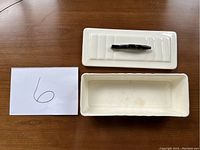 Top view of rectangular ceramic baking/serving dish with removable lid showing fish-shaped handle on lid and minor stains inside dish.