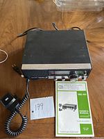 Realistic TRC-431 CB radio unit with microphone and owner's manual on wooden surface.