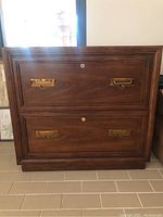 Front view of dark solid wood filing cabinet showing two drawers with brass handles and locks.
