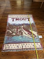 Top view of the fishing themed blanket showing fisherman, large jumping trout, mountains, and measuring tape along blanket length.