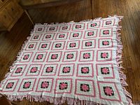 Full view of large knitted afghan blanket laid out on the floor, showing pink rose motif squares with pink fringes all around.