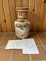 Front view of large ceramic vase with intricate Asian-inspired decorations and 50 number paper cards in front.