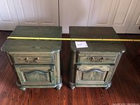 Pair of vintage green stained pine bedside tables side by side with a tape measure across the tops roughly showing width of one table.