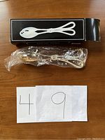 Silver plated salad tongs inside original packaging, wrapped in plastic, showing bracelet style handle design and tong heads.