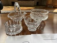 Four small crystal dishes shown on wooden surface with light background indoors.