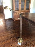 Full view of vintage brass floor lamp with adjustable arm on wooden floor.