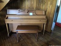 Full view of the vintage Cecilian wood upright piano with matching bench on wooden floor and wood-paneled wall background.