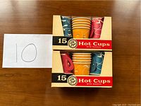 Two unopened 15-pack boxes of vintage Lily brand disposable paper hot cups with handles, stacked one on top of the other showing colorful cups with abstract patterns.