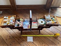Open vintage wooden sewing basket on legs showing fully extended trays and compartments with sewing supplies inside