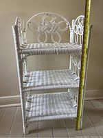 Front and side view of vintage white rattan 3 tier shelf, showcasing decorative knot detail on the sides and three woven rattan shelves. Measurement tape is visible for scale.