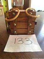 Front view of the vintage wooden treasure chest coaster box showing rope handles and metal studs.