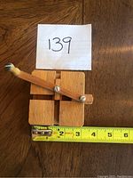 Top-down view of a vintage wooden desk toy with a wooden handle and screw fasteners, placed on a wood surface measuring approximately 4 inches in length.