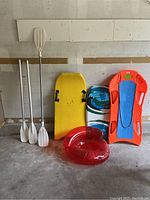 Full lot shot showing paddles, bodyboards, kneeboard, and inflatable ring against wall.