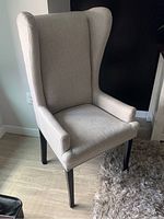 Photo of wingback arm chair with off white/beige fabric upholstery showing its profile and details of legs and armrests.
