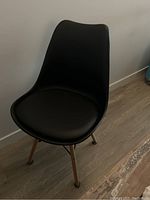 Black modern plastic molded chair with padded seat cushion, wooden legs, and metal support bars.