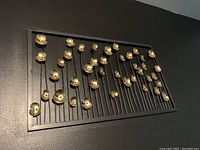 Black rectangular metal wall frame with gold flower-shaped decorations mounted on thin black stems inside the frame against a dark wall.