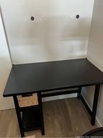 Photo of black desk with beige woven basket on built-in shelf under the desktop, showing overall design and condition.