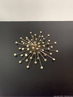 Front view of gold starburst wall decor showing circular disks on radiating rods mounted on a dark wall.