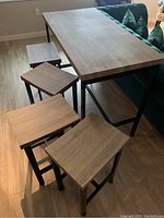 High dining table with four matching stools beside a green couch on wood floor